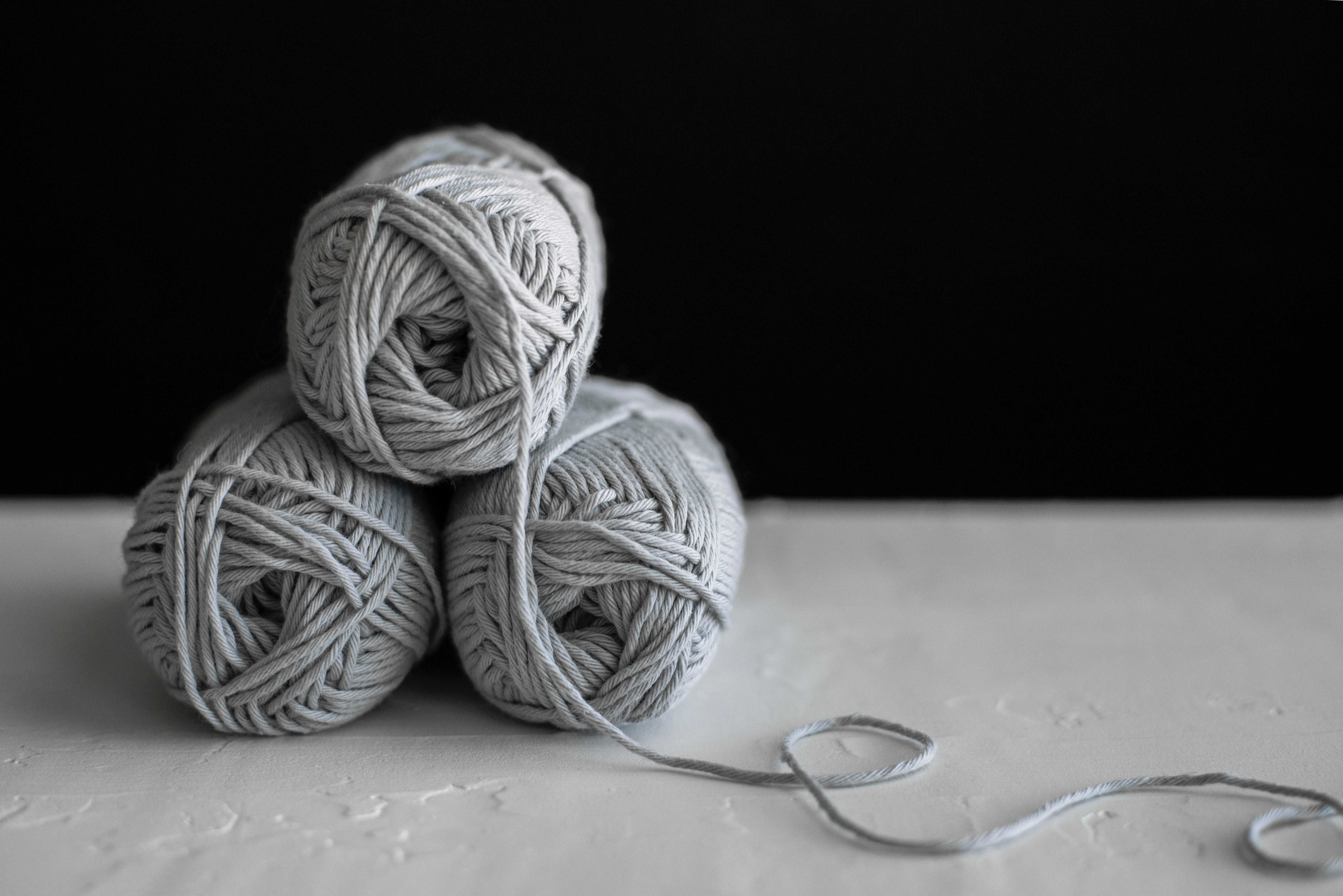 3 balls of Grey yarn on a white surface and a black background