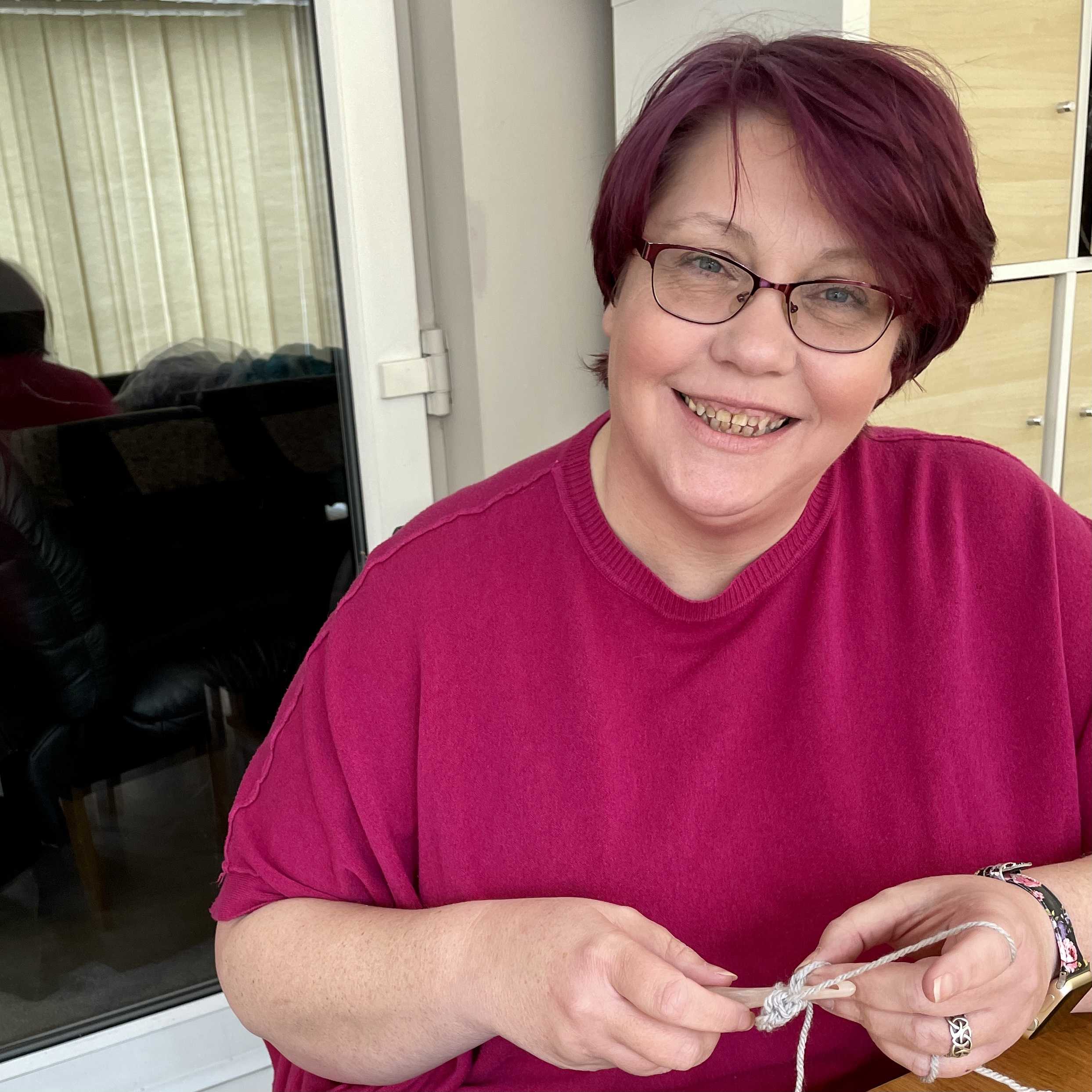 Keely in a pink top sitting at a table crocheting